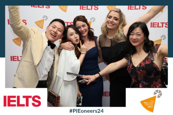 Five people pose happily for a group photo at the PIEoneer Awards 2024, captured with event photo printing on the spot, against an IELTS backdrop and hashtag #PIEoneers24 visible.
