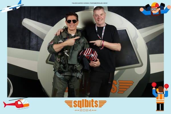 Two individuals standing in front of an aircraft-themed backdrop at the SQLBits 2024 event. One is dressed as a pilot with sunglasses, the other in a black shirt, both smiling for the camera.