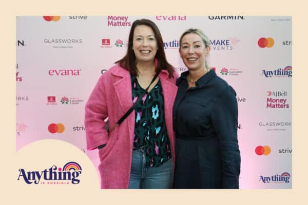 Two women smiling in front of a branded event backdrop with various logos and a slogan "Anything is Possible" in the corner capture the moment with on-site instant photo printing, adding an extra layer of excitement to the occasion.